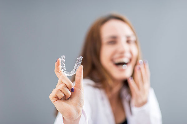 woman smiling while holding her Invisalign clear aligner